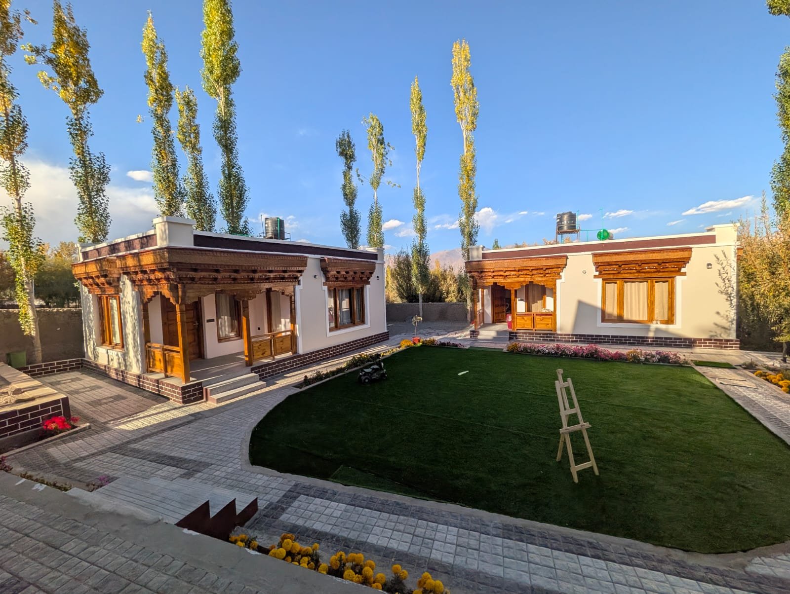The premium cottages around a green lawn, with tall poplars and blue Ladakh sky